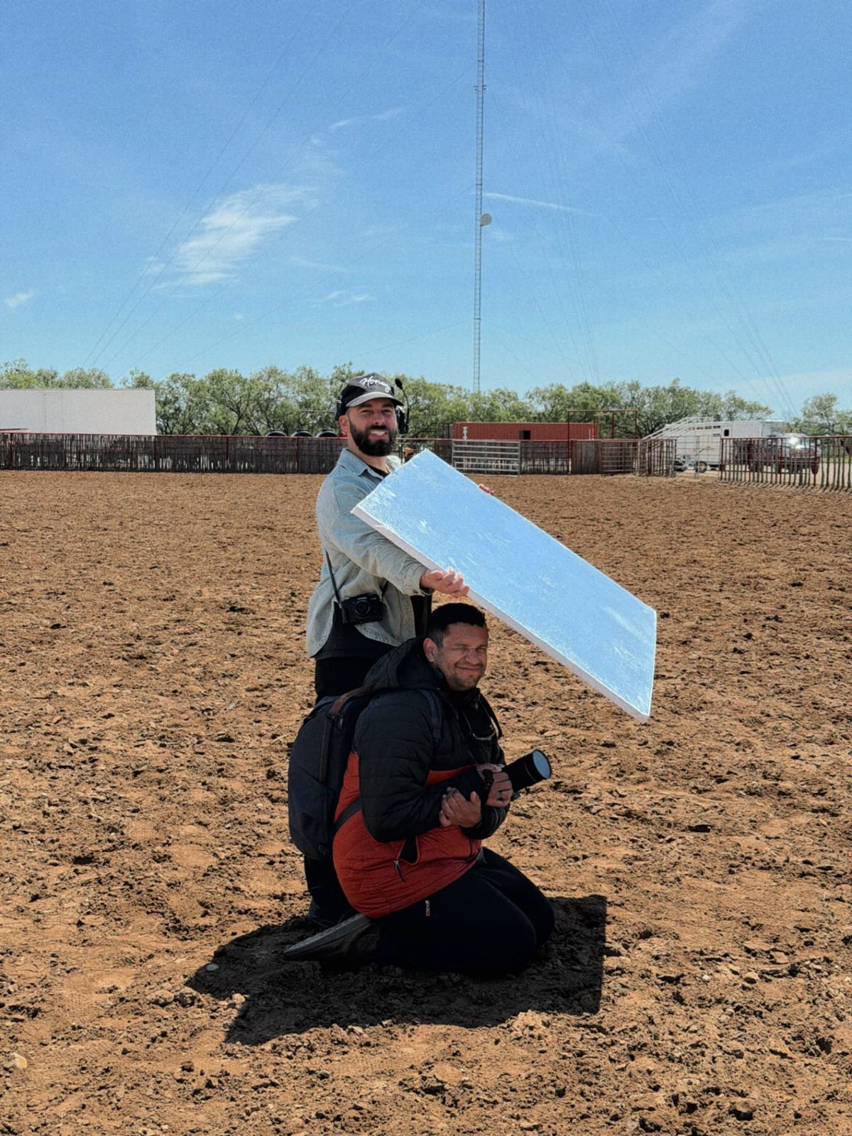 Crew holding a bounce over a kneeling operator in a dirt arena